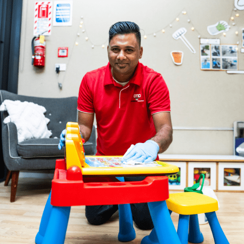 "Cleaner carefully sanitizing children's desks to ensure a safe and hygienic environment in an Auckland childcare center, meeting 2026 ECE hygiene standards." 