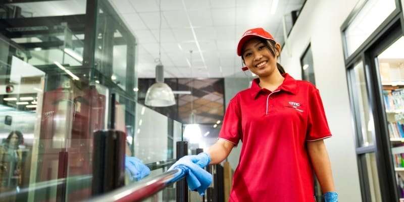 Cleaner in uniform sanitisin handle and smiling in office worskpace site in auckland